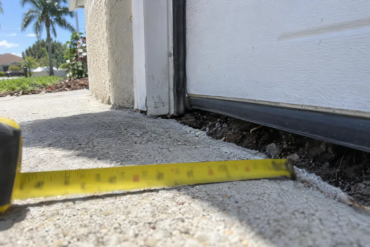 A garage floor slab dropped away from the door frame with a tape measure