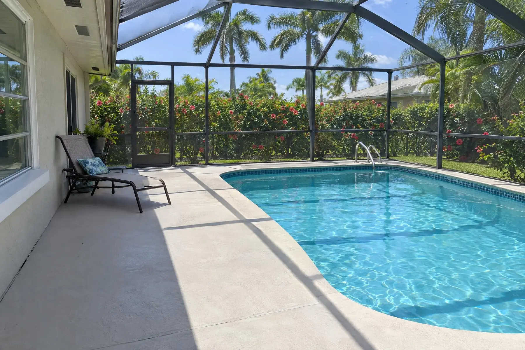 A level concrete pool deck beside a screened pool with a lounge chair